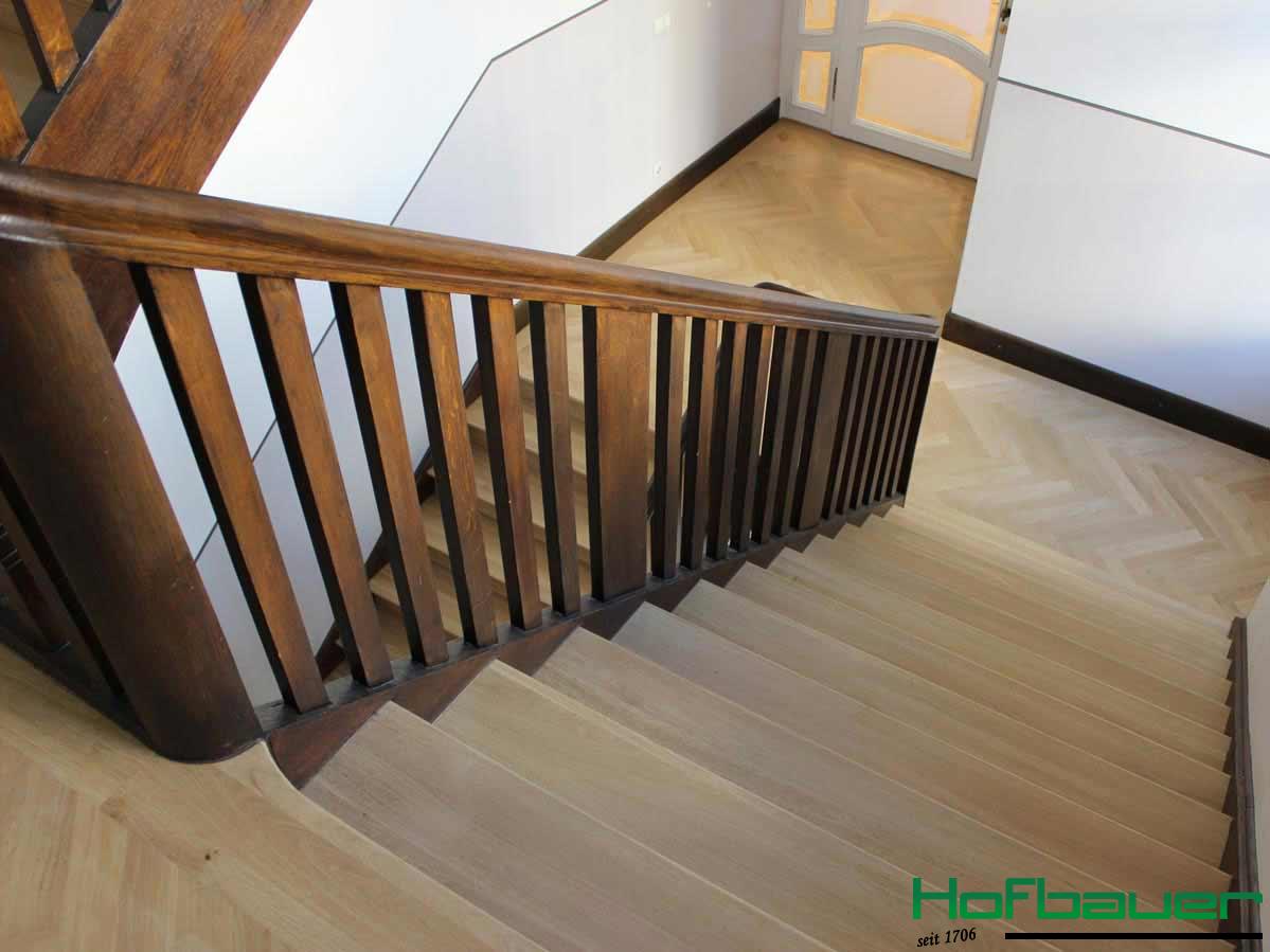 Treppenhaus aus seitlicher Vogelperspektive: Das Treppengeländer ist aus dunklem Holz, während die Treppen in hellem Holz mit Fischgrätenoptik im Treppenabsatz gestaltet sind