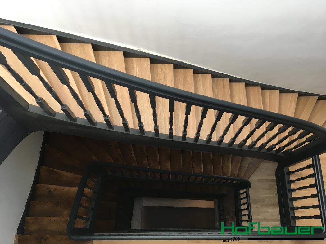 Treppenhaus aus der Vogelperspektive: Das Treppengeländer ist aus dunklem Holz, und die Treppen bestehen aus hellem Holz