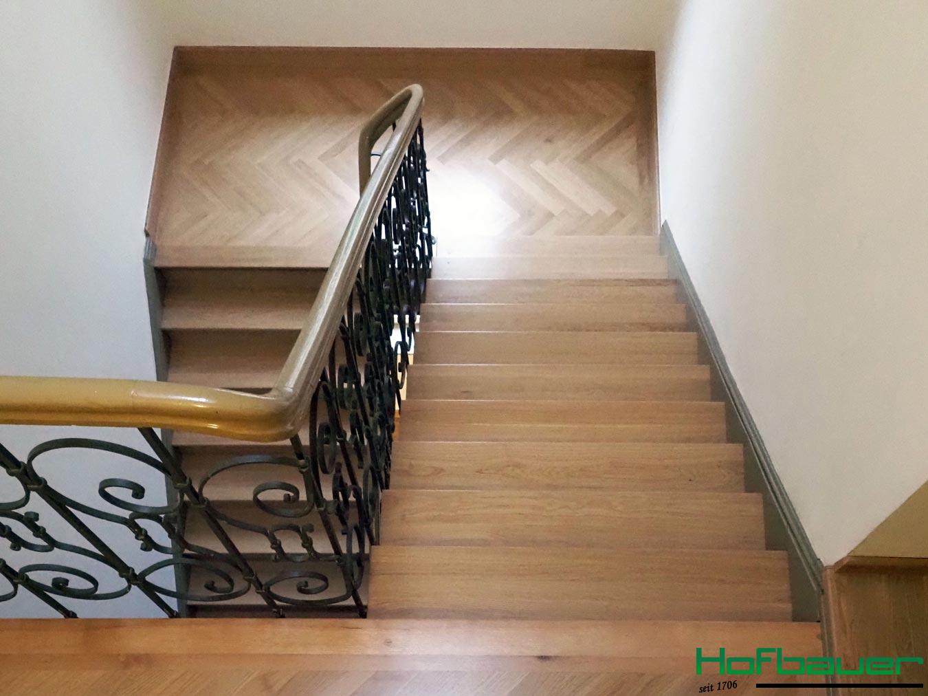 Hausflur aus der Vogelperspektive: Eine neue, helle Massivholztreppe in Fischgrätenoptik mit dazugehörigem Treppengeländer und schwarzen Metalldetails