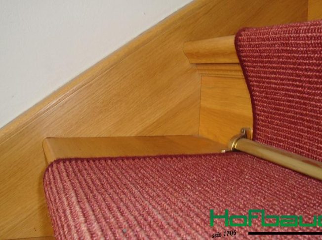 hofbauer-treppen-neustufen08_0 Nahaufnahme einer hellen Massivholztreppe mit roten Teppich und goldenen Teppichleistenhaltern